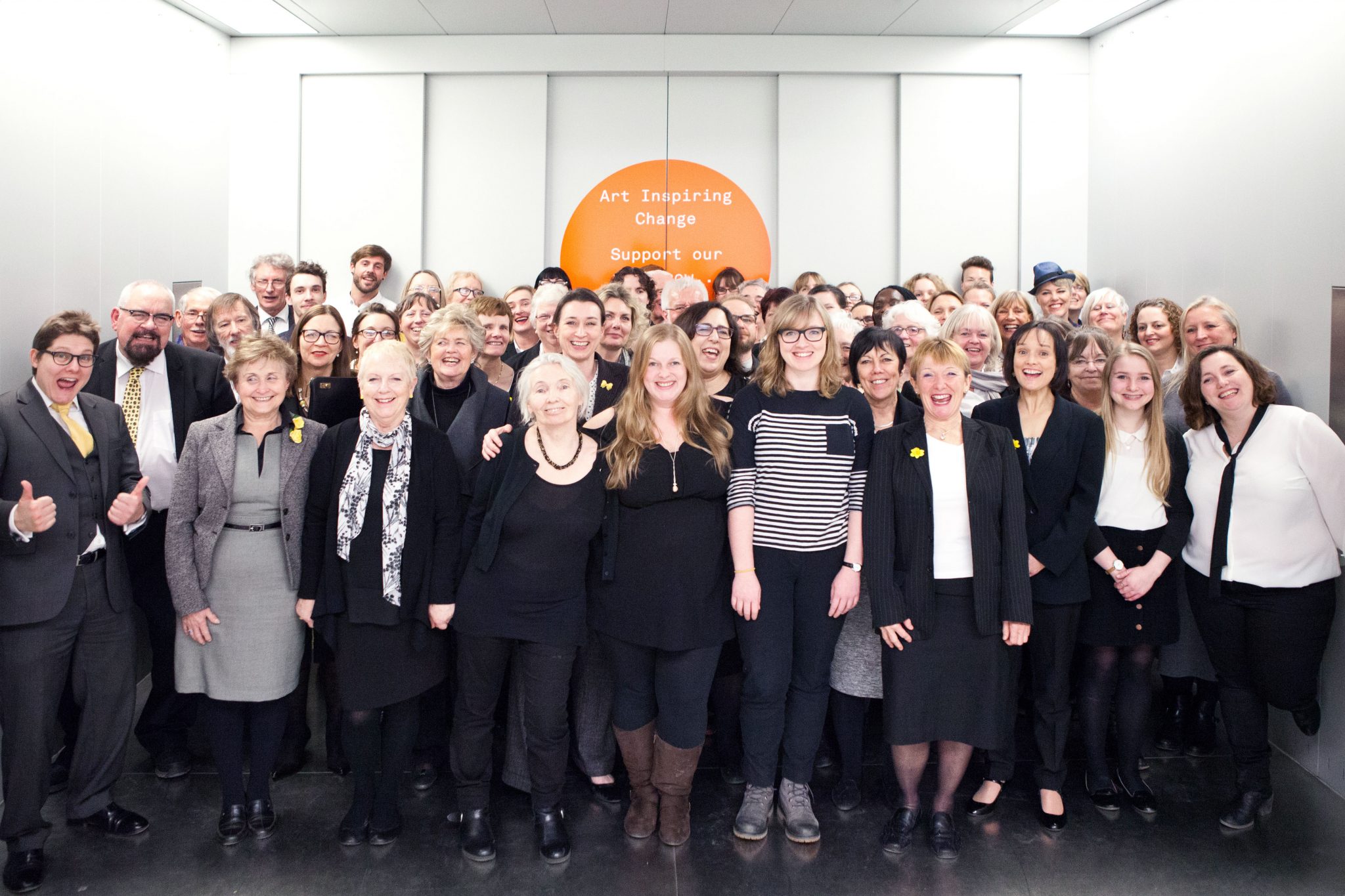 The LIFTED choir and Emily Peasgood stand inside the lift at Turner Contemporary, smiling at the camera.